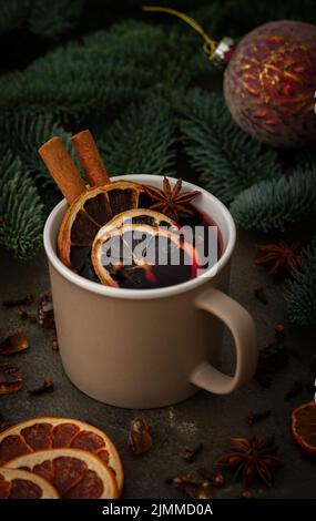 Bebida alcohólica caliente de Navidad vino caliente en una taza con cítricos, especias aromáticas y canela entre las ramas de abeto Foto de stock