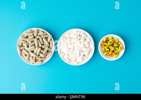 Fondo turquesa de un gran grupo de cápsulas variadas, píldoras y tabletas en cuencos blancos seguidos Foto de stock