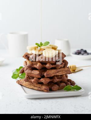 Gofres de plátano de chocolate con jarabe de arce en mesa blanca, vista lateral, vertical. Desayuno-almuerzo dulce Foto de stock