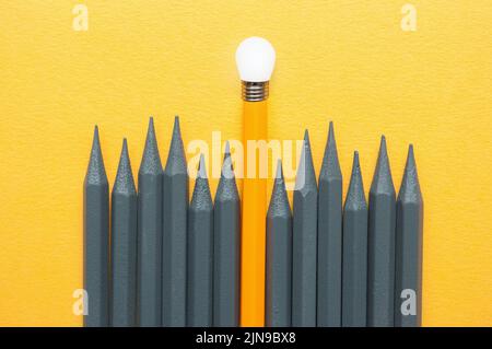 Lápiz naranja que destaca entre lápices grises con punta de bombilla, concepto de éxito de ideas únicas Foto de stock