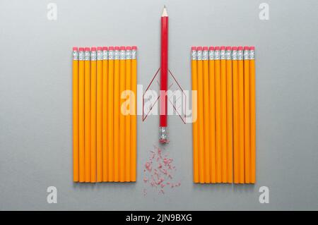 Lápiz rojo con boceto de cohete que sobresale entre una fila de lápices naranjas Foto de stock