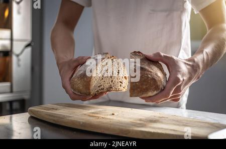 Un panadero macho corta pan recién horneado con un cuchillo para comprobar la calidad. Producción de productos de panadería como pequeña empresa. Foto de stock
