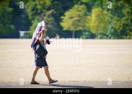 Una mujer se sombrilla en Hyde Park, Londres, cuando se ha declarado una sequía en algunas partes de Inglaterra después del verano más seco de los últimos 50 años. Fecha de la foto: Sábado 13 de agosto de 2022. Foto de stock
