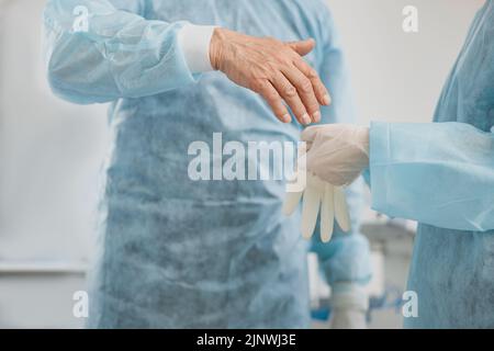 Primer plano de las manos del cirujano Se coloca guantes en el quirófano para prepararse para la cirugía Foto de stock