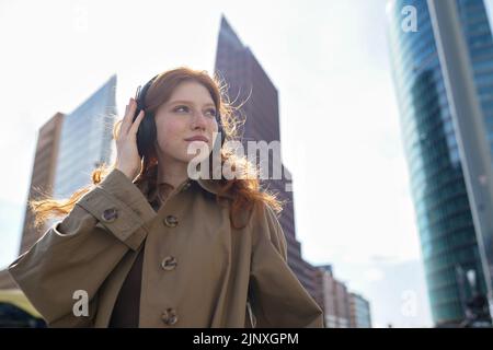 Adolescente pelirroja usando auriculares escuchando música en la gran ciudad. Foto de stock