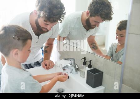 Asegurarse de que se laven las manos correctamente. Un padre joven y guapo que ayuda a su adorable niño a lavarse las manos en el baño en casa. Foto de stock