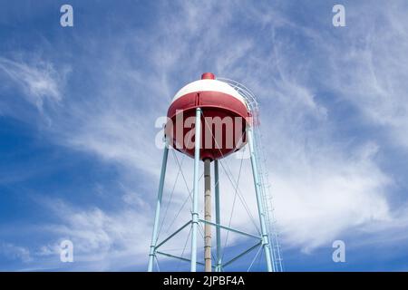 Vista hacia arriba de una torre de agua roja y blanca con forma redonda que se asemeja a un bogber de pesca, con el fondo azul del cielo Foto de stock