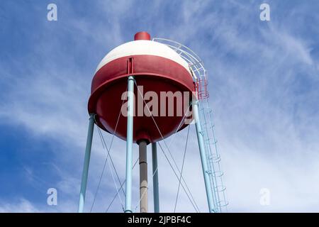 Vista hacia arriba de una torre de agua roja y blanca con forma redonda que se asemeja a un bogber de pesca, con el fondo azul del cielo Foto de stock