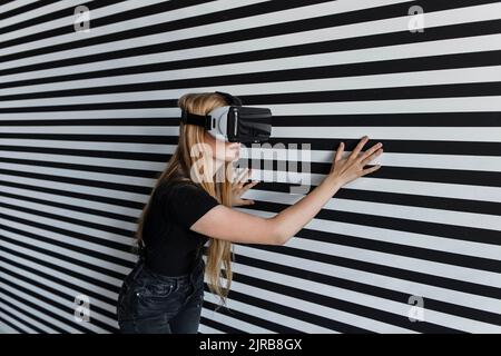 Chica con auriculares de realidad virtual tocando la pared a rayas Foto de stock