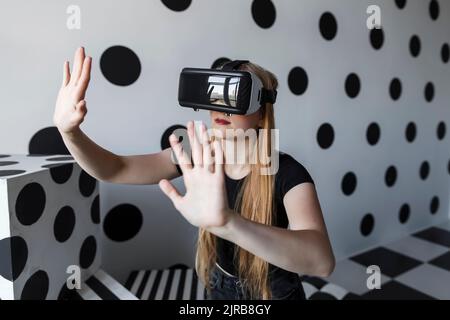 Chica haciendo gestos con auriculares de realidad virtual en la pared Foto de stock