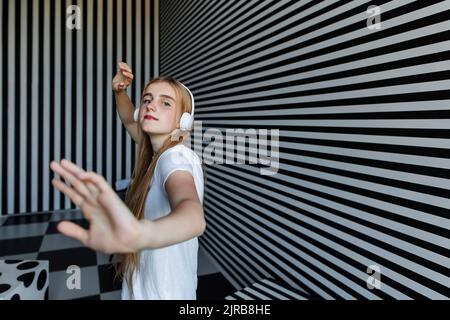 Chica adolescente con auriculares bailando por la pared a rayas Foto de stock