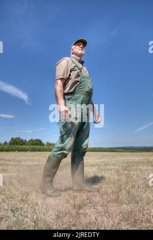 Un granjero camina a través de su pradera seca y mira el cielo con preocupación. Foto de stock