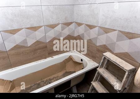 instalación de una bañera nueva y colocación de baldosas de cerámica en el baño. Reparar Foto de stock