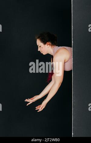 Una hermosa morena mira desde detrás de una pantalla negra. El retrato de estudio de una mujer joven realiza movimientos suaves con sus manos. Concepto para cosmeti Foto de stock