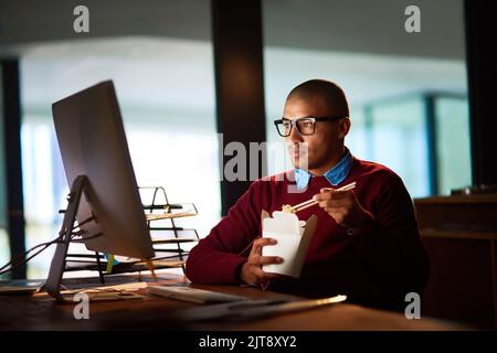 La comida es la clave para tener éxito en los turnos de noche. Un joven guapo que come comida china mientras trabaja tarde en su oficina. Foto de stock