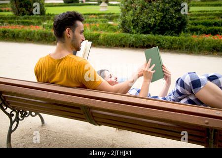 Volver de una pareja en un banco leyendo libros en una pose relajada en un parque Foto de stock