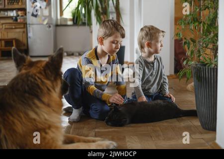 Los niños jugando, acariciando el gato negro mientras el perro pastor alemán está sentado cerca de casa. Los niños tienen mascotas y se ocupan de ellas
