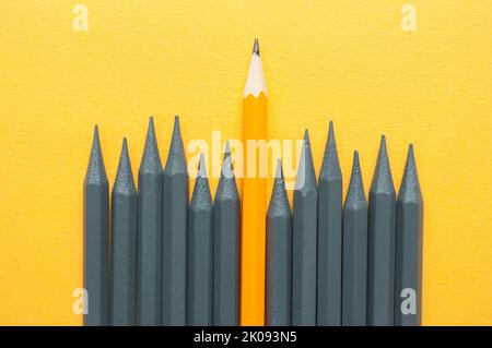 Lápiz naranja que sobresale entre lápices grises Foto de stock