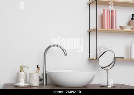 Lavabo moderno y accesorios de baño en la mesa cerca de la pared blanca Foto de stock