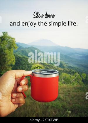 Cita motivacional inspiradora - Relájese y disfrute de la vida sencilla. Con una persona sosteniendo una taza roja de café o té caliente en el fondo de la montaña de la naturaleza Foto de stock
