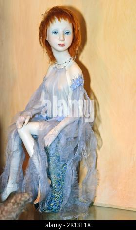 Una muñeca coleccionable, niña de pelo rojo en capa ligera, está en exhibición en la exposición de la Edad del Ángel de las muñecas del autor en Kiev, Ucrania. Foto de stock