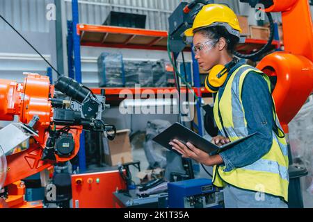 Adolescente africana joven ingeniera trabajadora trabajando en una avanzada fábrica robótica con seguridad Foto de stock