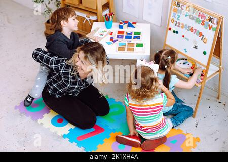 Maestro con niños divirtiéndose y jugando juegos, aprendiendo letras y números en el centro de desarrollo infantil Foto de stock