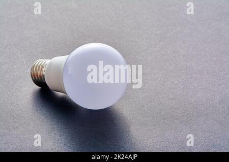 Una lámpara LED blanca con una base E27 descansa sobre un fondo gris. Fotografía de alta calidad Foto de stock
