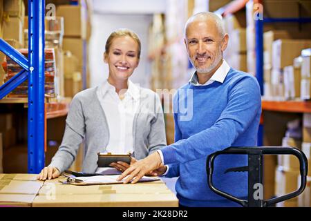 Su pedido llegará a tiempo cada vez. Retrato de un hombre y una mujer inspeccionando el inventario en un gran almacén de distribución. Foto de stock