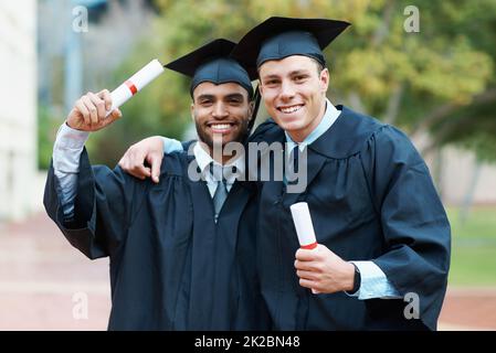 Estábamos en camino al éxito. Dos jóvenes graduados universitarios que llevan sus diplomas mientras usan gorra y bata. Foto de stock