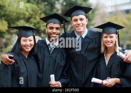 Estudiantes y compañeros graduados. Un grupo de graduados universitarios de pie en gorra y vestido y sosteniendo sus diplomas. Foto de stock