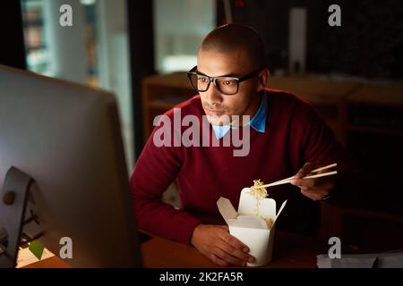 La comida para llevar es la clave para trabajar tarde. Tiro de un hombre joven guapo comiendo comida china mientras trabajaba tarde en su oficina. Foto de stock