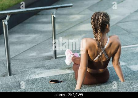 Mujer sentada en escaleras de hormigón después de hacer ejercicio al aire libre