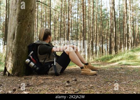 Hiker femenino durante la parada pequeña sentada en el suelo en el bosque verde