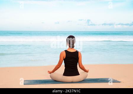 mujer que practica yoga en la orilla del mar de la playa tropical, mujer joven que medita en la playa hacer ejercicios de yoga Foto de stock