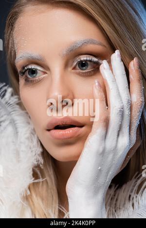 retrato de joven rubia con maquillaje de invierno tocando la cara con la mano en pintura blanca,imagen de archivo Foto de stock
