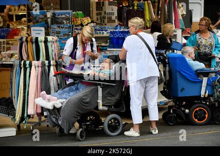 Lourdes, Hautes-Pyrénées, Francia. Cuidadores con un inválido visitando las tiendas de souvenirs Foto de stock