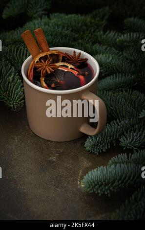 Bebida alcohólica caliente de Navidad vino caliente en una taza con cítricos, especias aromáticas y canela entre las ramas de abeto Foto de stock