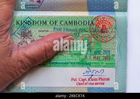 Mano con pasaporte abierto con el Reino de Camboya Visa en pasaporte británico Foto de stock