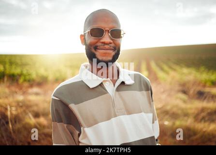 Moda, granja y la agricultura con un hombre negro agricultor al aire libre en el sol de verano en gafas de sol. Sostenibilidad, agricultura y estilo con un joven guapo Foto de stock