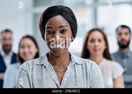 Liderar un equipo dedicado a su próximo gran éxito. Retrato de una mujer de negocios de pie en una oficina con sus colegas en el fondo. Foto de stock