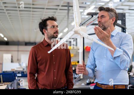 Un hombre de negocios maduro que sostiene un aerogenerador conversando con un compañero del almacén Foto de stock