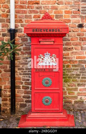 De pie viejo buzón rojo contra una pared de piedra de una antigua casa en el centro de Deventer. Foto de stock