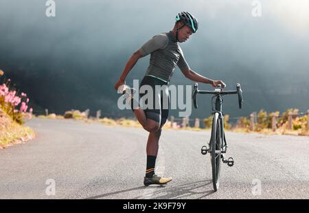 Estiramiento de piernas, fitness y hombre en bicicleta en una carretera con  una bicicleta en las montañas para cardio, viajes y ejercicios deportivos  en la naturaleza. Atleta haciendo un cálido Fotografía de