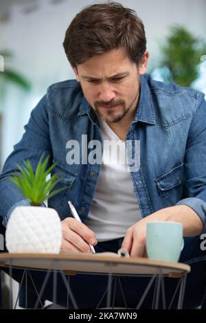 hombre joven escribiendo una nota en el sofá Foto de stock
