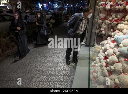 Un hombre iraní que lleva una máscara protectora mira a una tienda decorada para el día de San Valentín en el centro de Teherán, en medio del brote de COVID-19 en Irán, mientras dos mujeres con velo caminan a lo largo de una calle el 12 de febrero de 2021. (Foto de Morteza Nikoubazl/NurPhoto) Foto de stock
