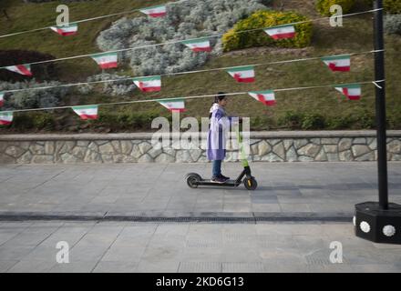 Una joven iraní monta una moto junto a las banderas de Irán en el Jardín del Museo de Arte en el norte de Teherán durante una ceremonia para conmemorar el Día Nacional de la República Islámica de Irán el 1 de abril de 2022. El pueblo iraní votó sí en un referéndum por el régimen de la República Islámica hace cuarenta y tres años. (Foto de Morteza Nikoubazl/NurPhoto)