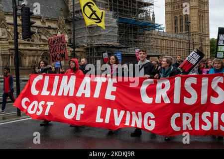 Extinción Rebelión activista con un estandarte 'Crisis climática, crisis de costo de vida' marchando fuera del Parlamento del Reino Unido. Foto de stock