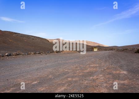Solitario camino desértico a través de un árido paisaje serpentea hacia montañas volcánicas en el horizonte, cerca de Playa Mujeres y la costa de Papagayo, Lanzarote, Ca Foto de stock