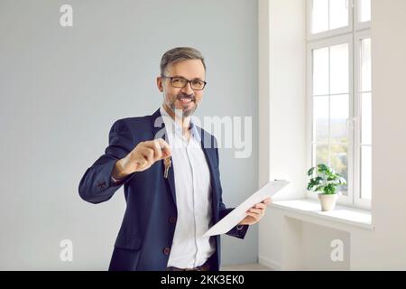 Retrato de amable agente de bienes raíces masculino mostrando la llave de la casa que se puede comprar o alquilar. Foto de stock